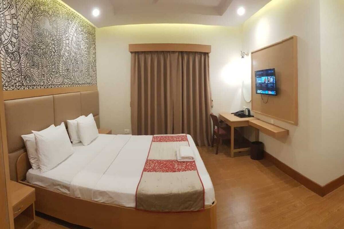 A hotel room with a large bed, a desk, a television, and a curtain.