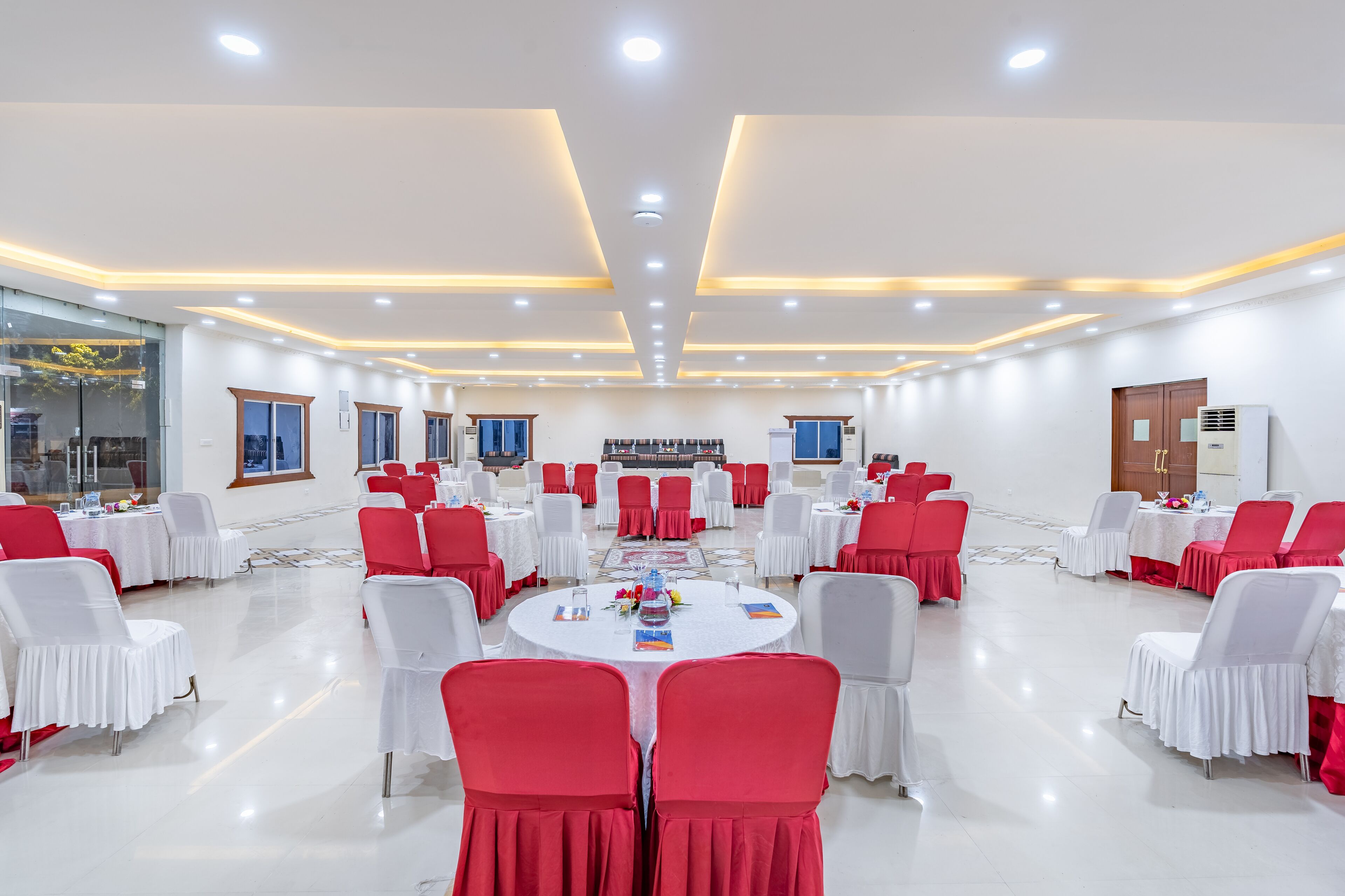 Une salle de conférence avec des chaises blanches et rouges, des tables rondes et un plafond au design moderne.