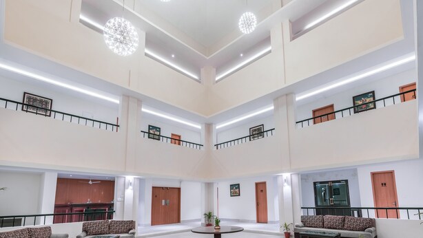 A spacious, multi-level lobby with a central round table, wooden doors, and a kitchen area in the background. - Mithila Yatri Niwas (Janakpur)