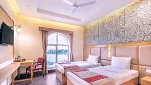 A hotel room with two beds, a desk, a chair, a TV, and a large window with a view of the city. - Mithila Yatri Niwas (Janakpur)