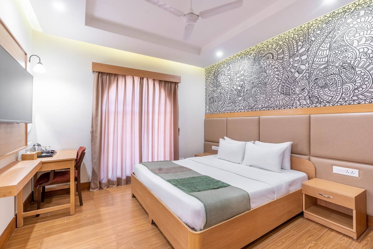 A hotel room with a bed, bedside table, desk, chair, and a large decorative wall.