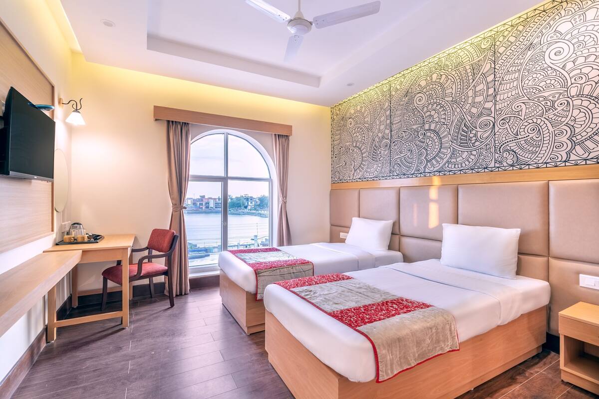 A hotel room with two beds, a desk, a chair, a TV, and a large window with a view.