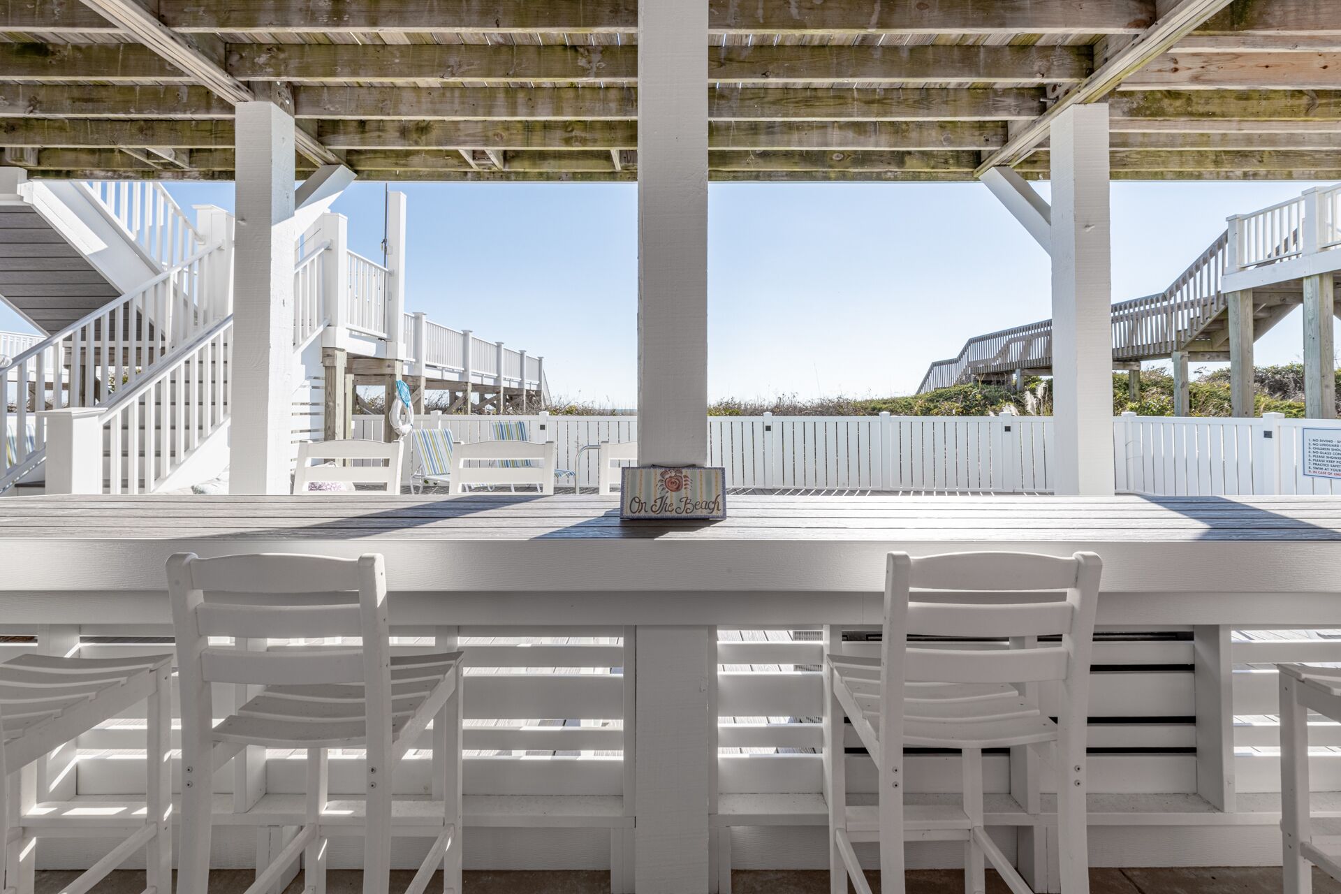 Een strandbar met witte houten meubels en een bord waarop staat 