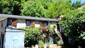 A rustic stone building with wooden shutters, a small garden with potted plants, and a staircase leading to a higher level. - A miller's house in the quiet countryside for 2 people, pets welcome (Montredon-Labessonnié)