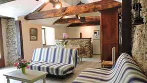 A cozy room with a striped sofa, a small table with a vase of flowers, and a kitchen in the background. - A miller's house in the quiet countryside for 2 people, pets welcome (Montredon-Labessonnié)