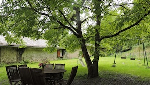 A wooden table and chairs set outdoors under a tree, with a grassy area and a slide in the background. - A miller's house in the quiet countryside for 2 people, pets welcome (Montredon-Labessonnié)