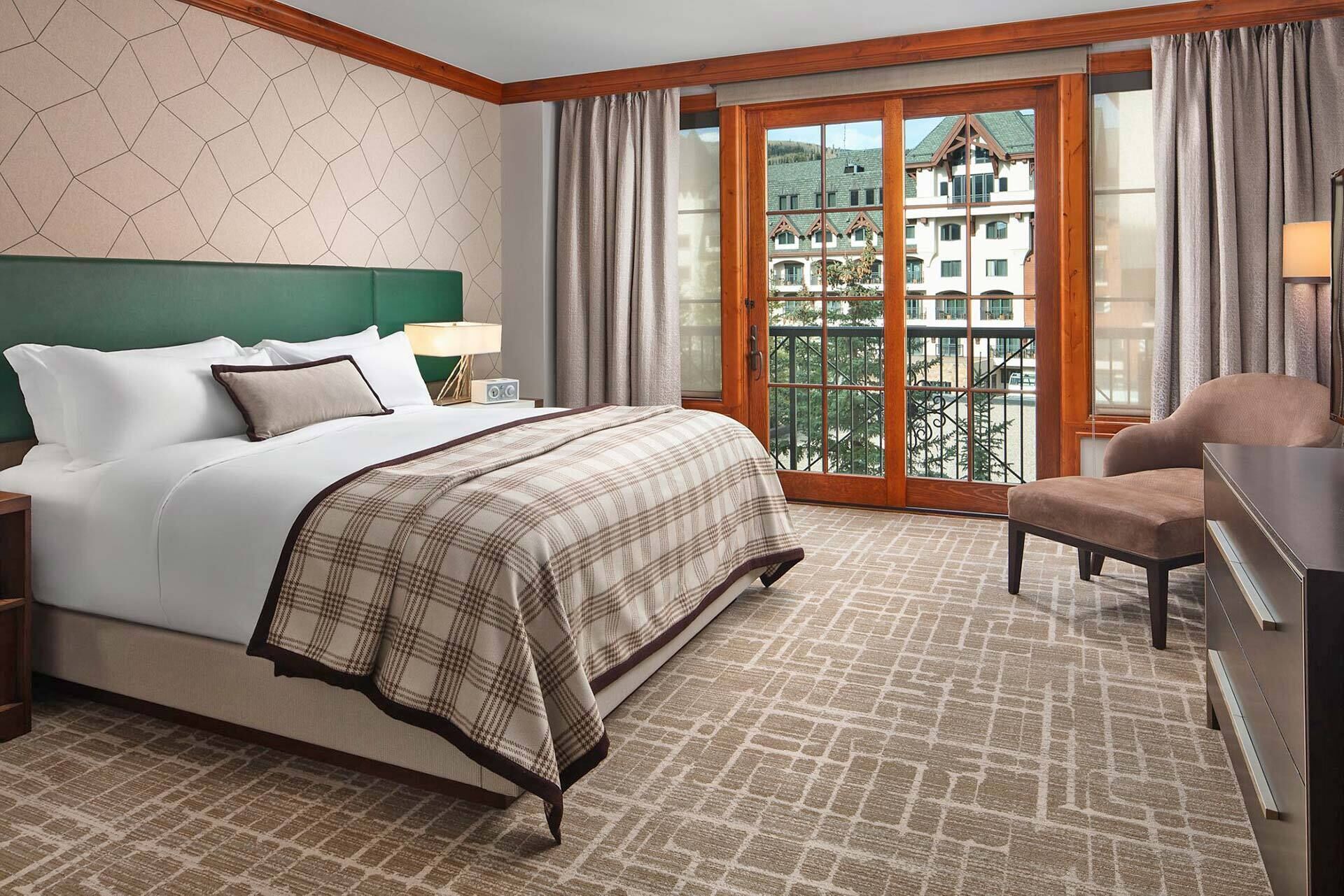 Une chambre d’hôtel avec un lit, une chaise, un bureau, une fenêtre donnant sur des immeubles et un sol à motifs.