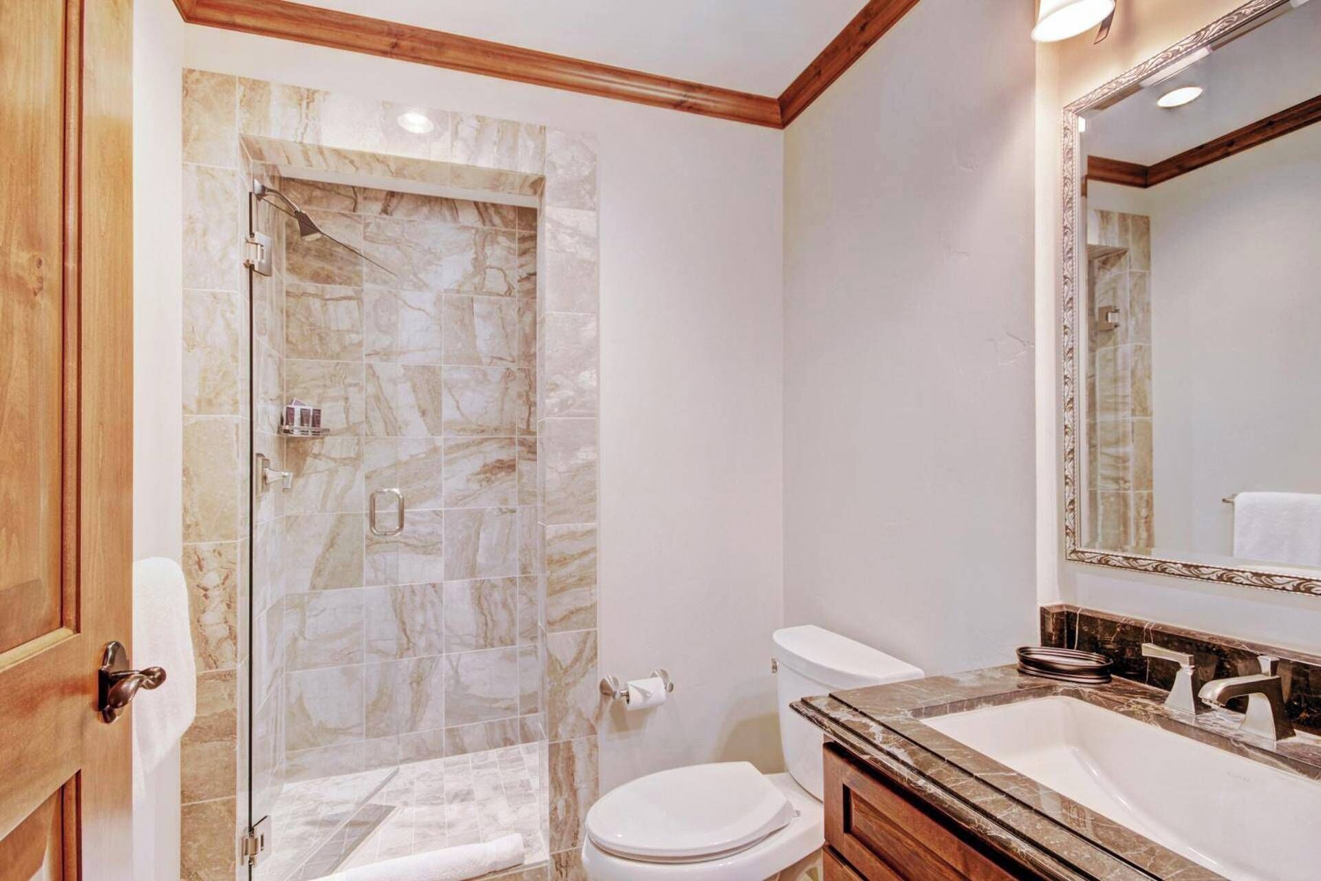Une salle de bain avec une douche à parois de verre, des toilettes blanches et un lavabo en marbre avec un miroir.