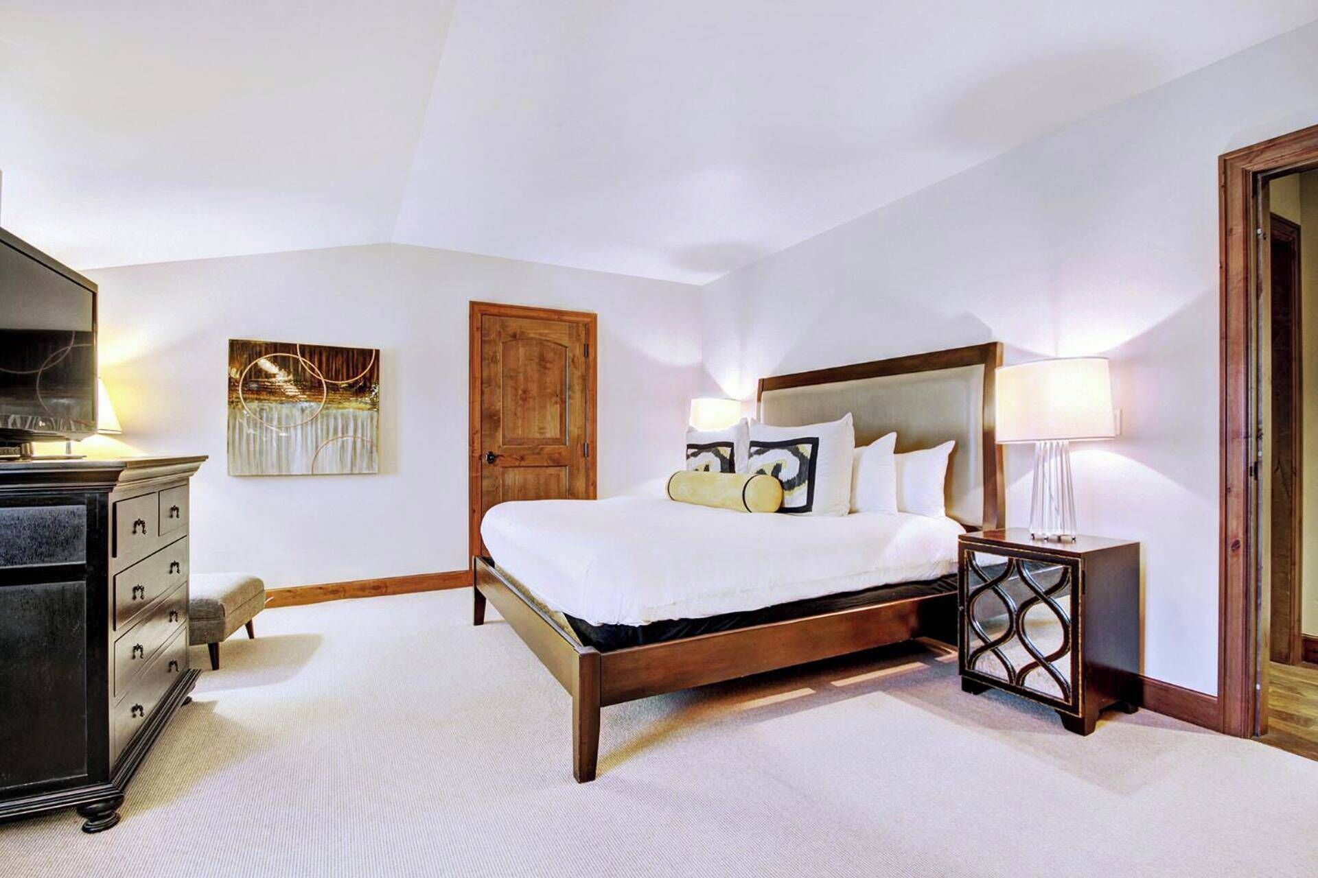 A hotel room with a large bed, a wooden wardrobe, a television, and a painting on the wall.