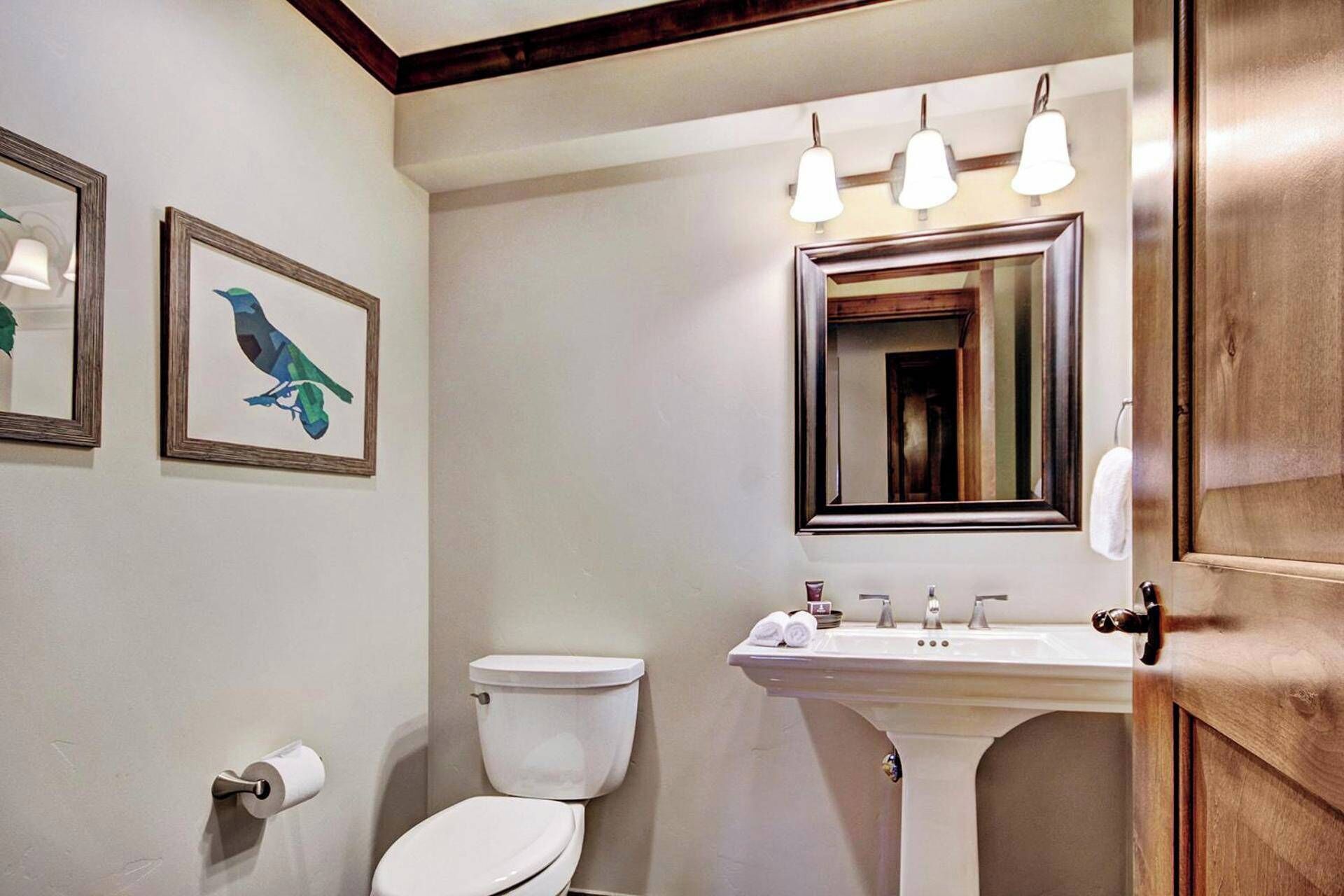 Une salle de bain avec des toilettes, un lavabo et un miroir. Des tableaux encadrés ornent le mur.