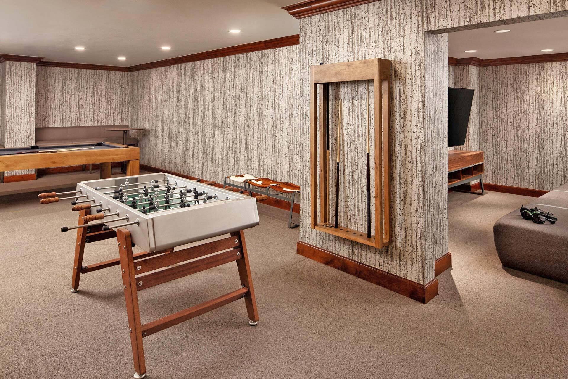 A room with a foosball table, a pool table, and a billiards table.