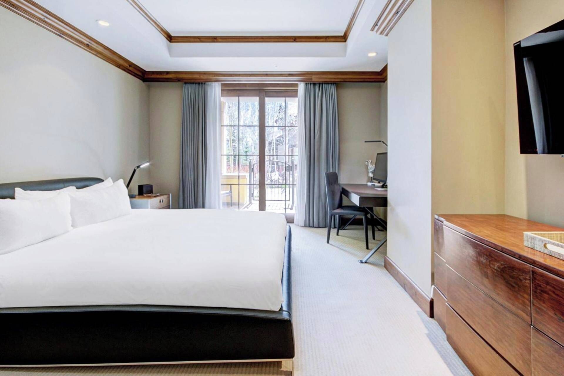 Une chambre d’hôtel avec un grand lit, un bureau, une chaise, une télévision et une fenêtre avec des rideaux.