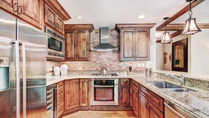 A modern kitchen with wooden cabinets, stainless steel appliances, granite countertops, and a central island.