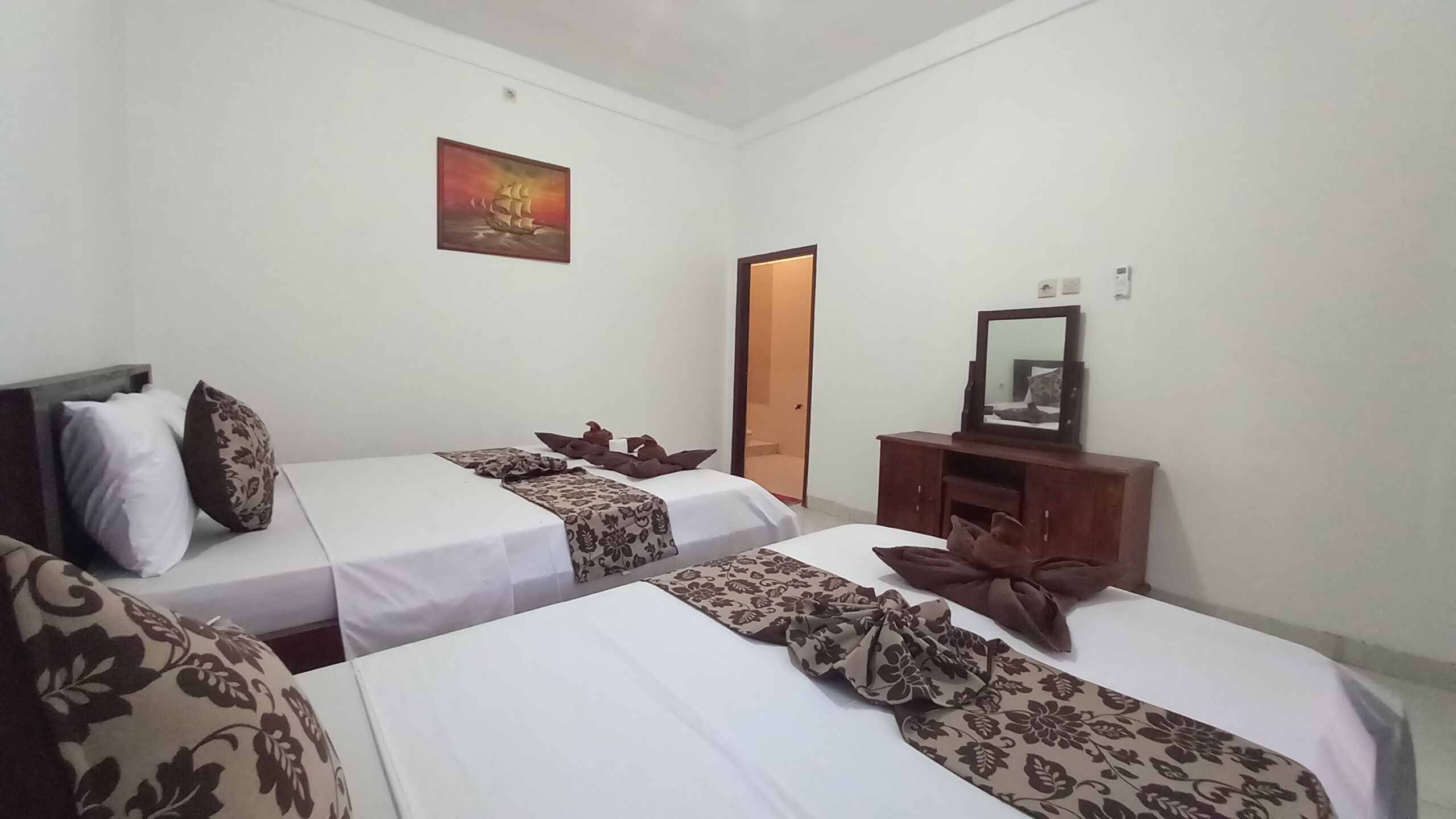 A hotel room with two single beds, a wooden dresser with a mirror, and a painting on the wall.