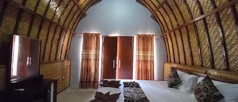 Een kamer met een hoog, gewelfd plafond, een bed met kussens en dekbed, een televisie op een houten standaard en een kledingkast.