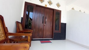 A wooden door with glass panels, a red mat on the floor, and a chair with a woven backrest. - Joevana Cottage (Gili Trawangan)