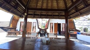 A covered outdoor area with a thatched roof, wooden benches, and a central decorative element. - Joevana Cottage (Gili Trawangan)