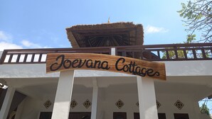 A sign for Joevana Cottages with a thatched roof and white walls. - Joevana Cottage (Gili Trawangan)