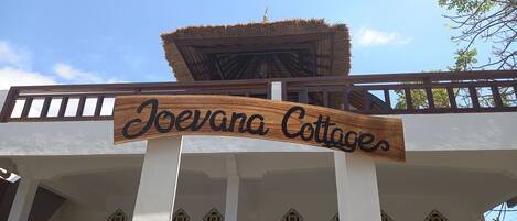 A sign for Joevana Cottages with a thatched roof and white walls.