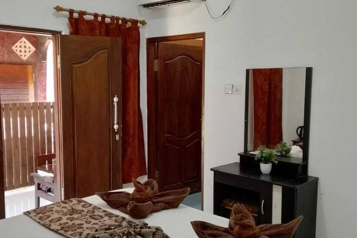 A hotel room with a bed, a desk with a mirror, and an air conditioning unit.