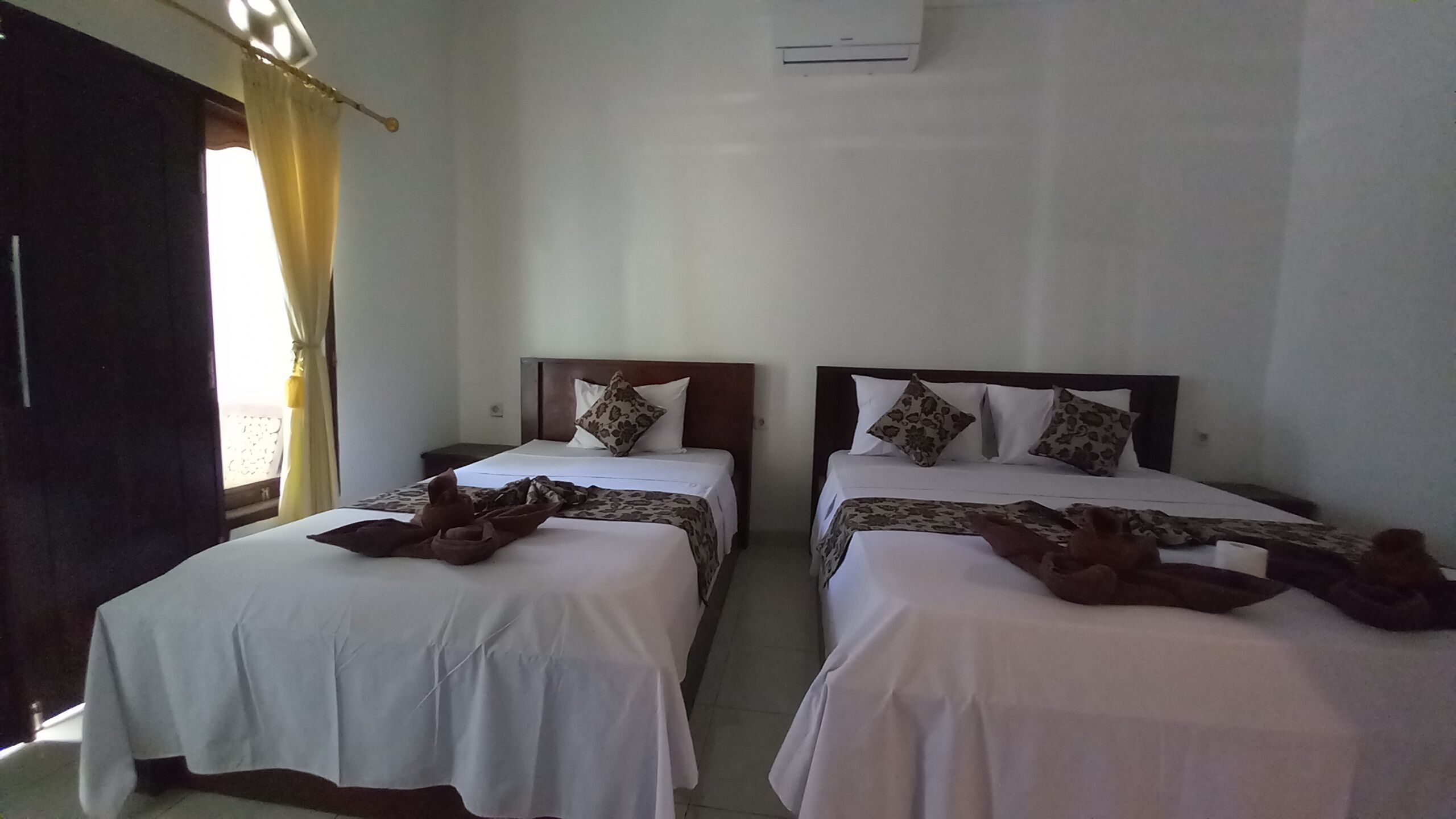 Ein Hotelzimmer mit zwei Betten, jeweils mit einem hölzernen Kopfteil, weißer Bettwäsche und gemusterten Zierkissen.