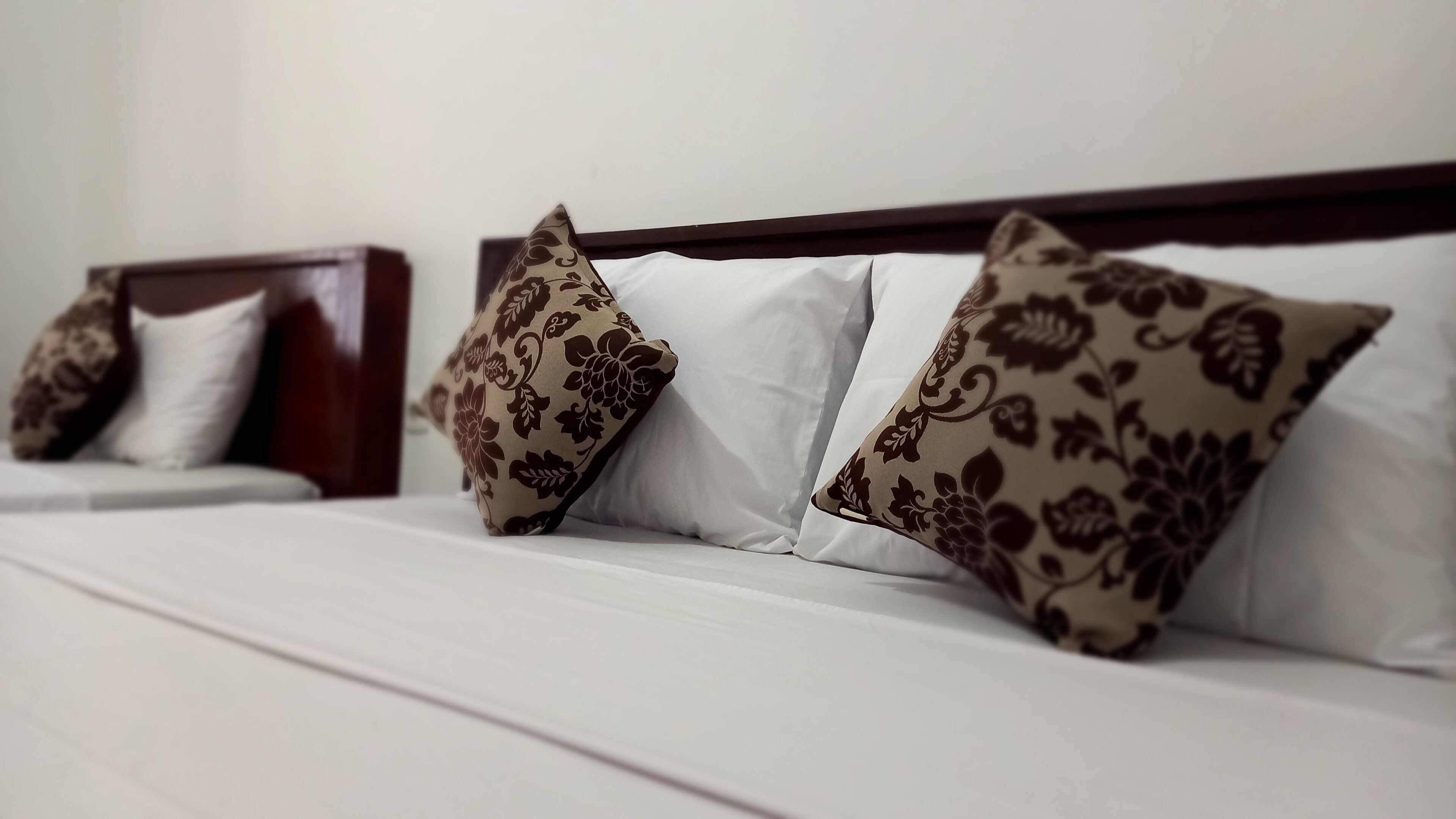 Una cama con sábanas blancas y dos almohadones estampados.