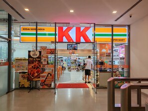 The entrance to a supermarket with a prominent 'KK' sign, glass doors, and promotional posters on the walls.