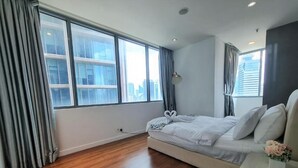 Ein modernes Schlafzimmer mit großem Fenster, einem Bett mit weißer Bettwäsche und einem kleinen Nachttisch mit Blumen in einer Vase.