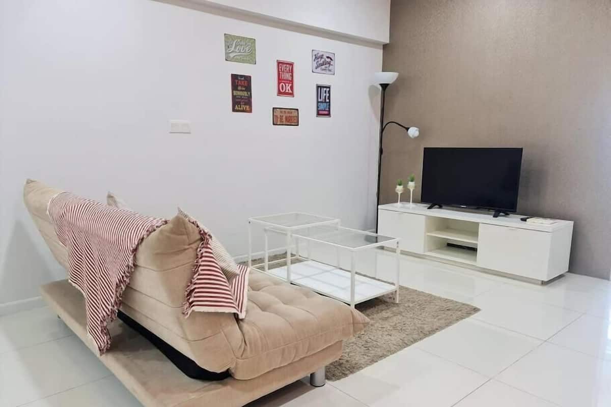 A modern living room with a beige sofa, a glass coffee table, a white TV stand, and motivational wall art.