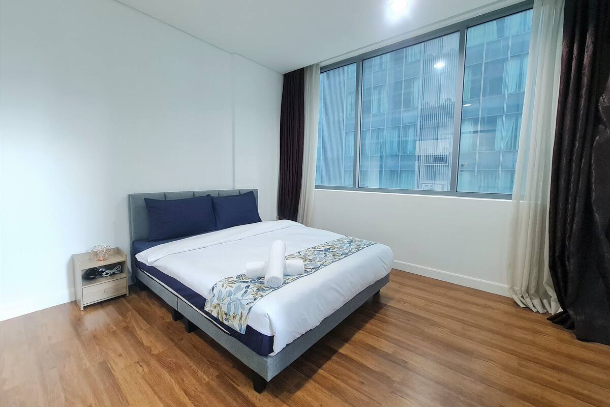 A neatly arranged bedroom with a bed, a nightstand, a window with curtains, and a view of the outside.