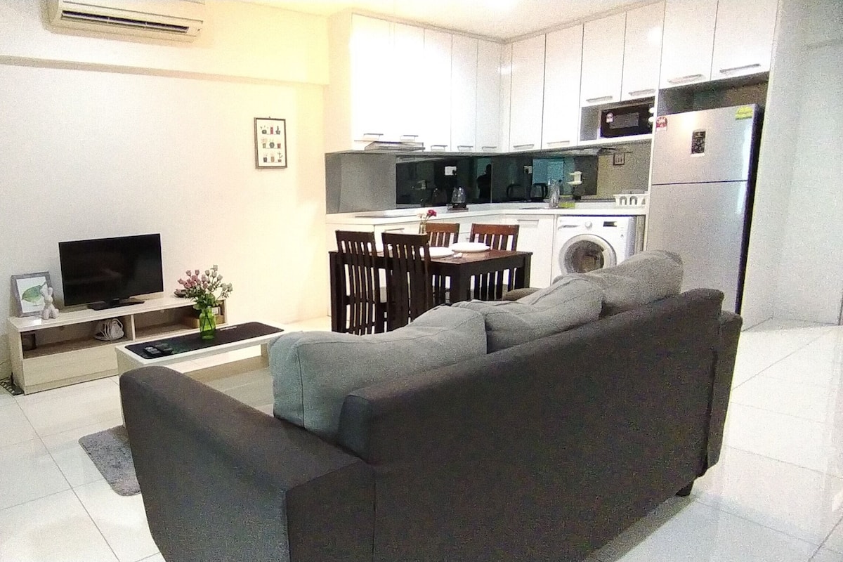 A modern living room with a grey sofa, a wooden chair, a flat-screen TV, and a dining area with a table and chairs.