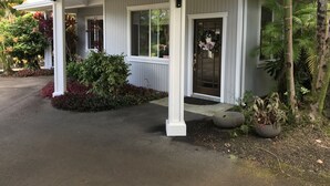 A covered porch with a door, white columns, and a small garden area with plants and a potted plant.