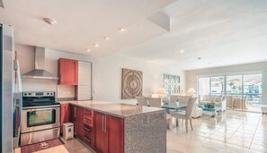 Una cocina moderna con electrodomésticos de acero inoxidable, encimera de granito y comedor con mesa y sillas de vidrio.