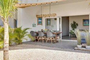 Un espace extérieur aménagé pour les repas, avec une table et des chaises, entouré de plantes et d’un palmier.
