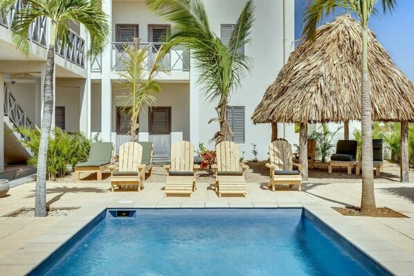A pool area with lounge chairs and a thatched roof structure.