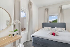 A bedroom with a bed, a bedside table, a mirror, and a window with curtains.