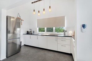 A modern kitchen with a stainless steel refrigerator, white cabinets, a black countertop, and pendant lighting. - Belnem Breeze Kas Gosa with a private garden and a rinse tank for your dive gear (Kralendijk)