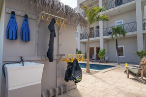 Uma área junto à piscina com um telhado de palha, uma banheira branca e uma bolsa preta pendurada em um suporte amarelo.
