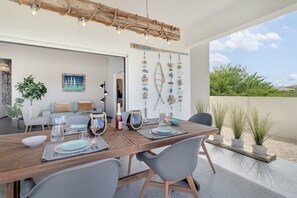 A dining area with a wooden table set for four, a hanging light fixture, and a view of the outdoors.