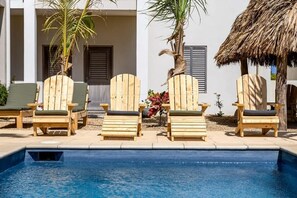 A poolside area with wooden lounge chairs and a thatched roof structure.