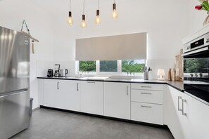 Une cuisine moderne dotée d’un réfrigérateur en acier inoxydable, de meubles blancs, d’une grande fenêtre et d’un plan de travail noir.