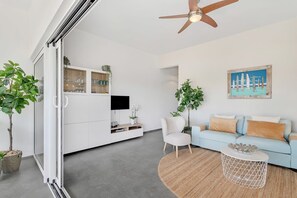 Uma sala de estar moderna com um sofá, uma mesa de centro e uma televisão sobre um armário branco.