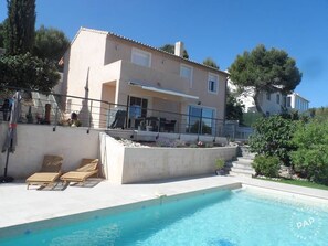 Une maison à deux étages avec une piscine, un espace salon extérieur et un jardin.