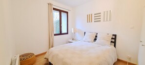A bedroom with a bed, a window with curtains, a bedside table, and wall art.