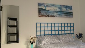 Een slaapkamer met een bed, een nachtkastje, een wandplank en een schilderij van een vuurtoren.