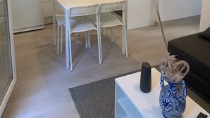 Een moderne keuken met witte kastjes, een eettafel met stoelen, een magnetron en een waterkoker.