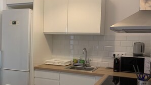 Een kleine keuken met witte kastjes, een ingebouwde magnetron en een spoelbak.