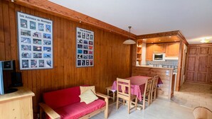 Ein gemütliches Zimmer mit Holzwand, einem roten Sofa, einem Esstisch mit Stühlen und einer Küchenzeile.