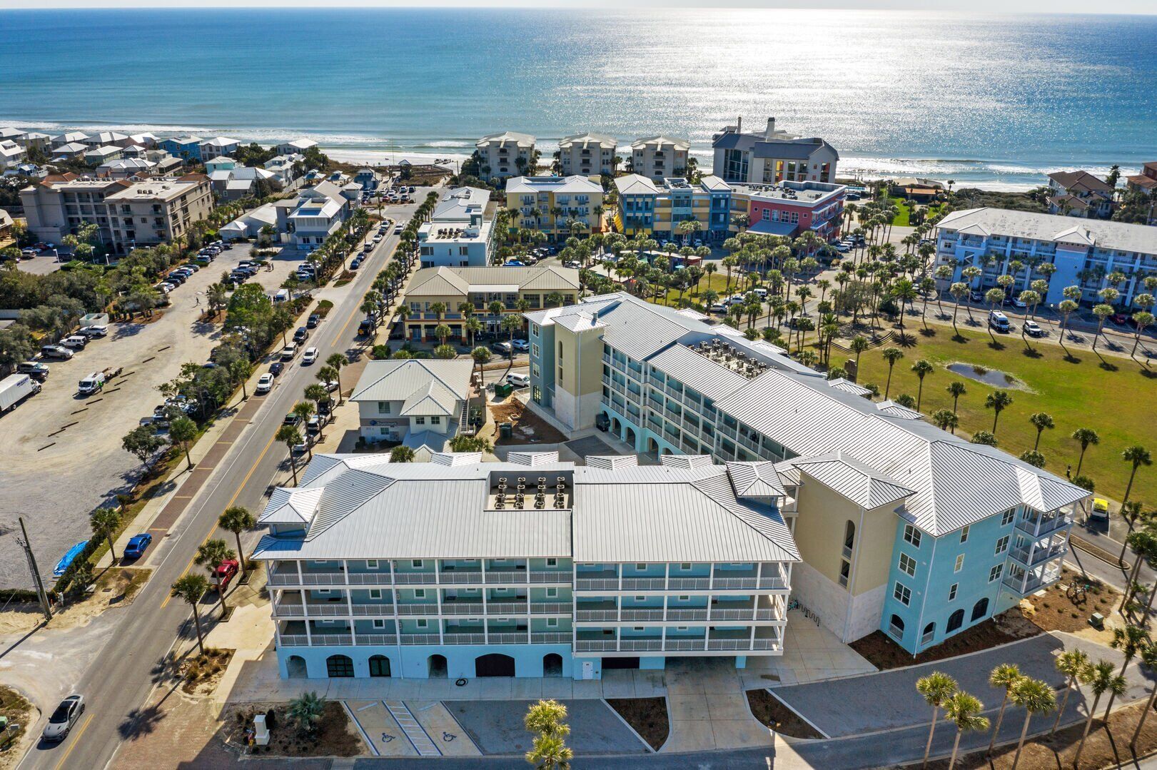 An aerial view of a coastal hotel complex with multiple buildings, parking areas, and a beachfront view.