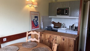 Une cuisine compacte avec une table à manger en bois, deux sets de table en fibres tressées, un four à micro-ondes et un évier.